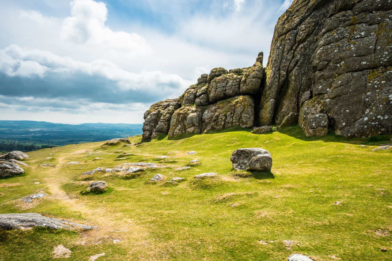 A granite tor above open moorland on Dartmoor, with Devon countryside stretching out below A granite tor above open moorland on Dartmoor, with Devon countryside stretching out below
