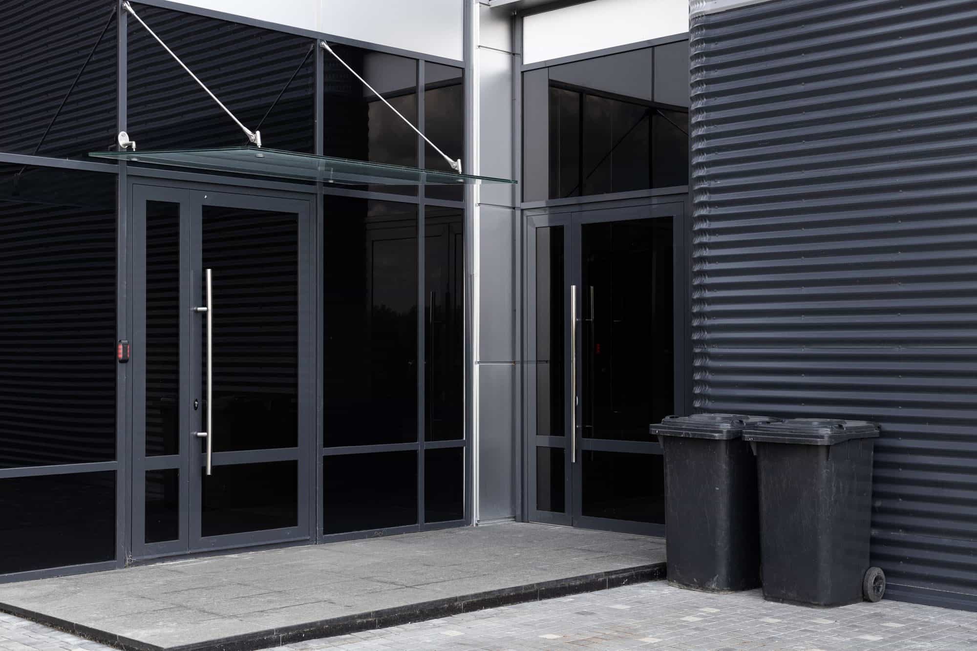Commercial wheelie bins beside the glass entrance of a modern business unit Commercial wheelie bins beside the glass entrance of a modern business unit