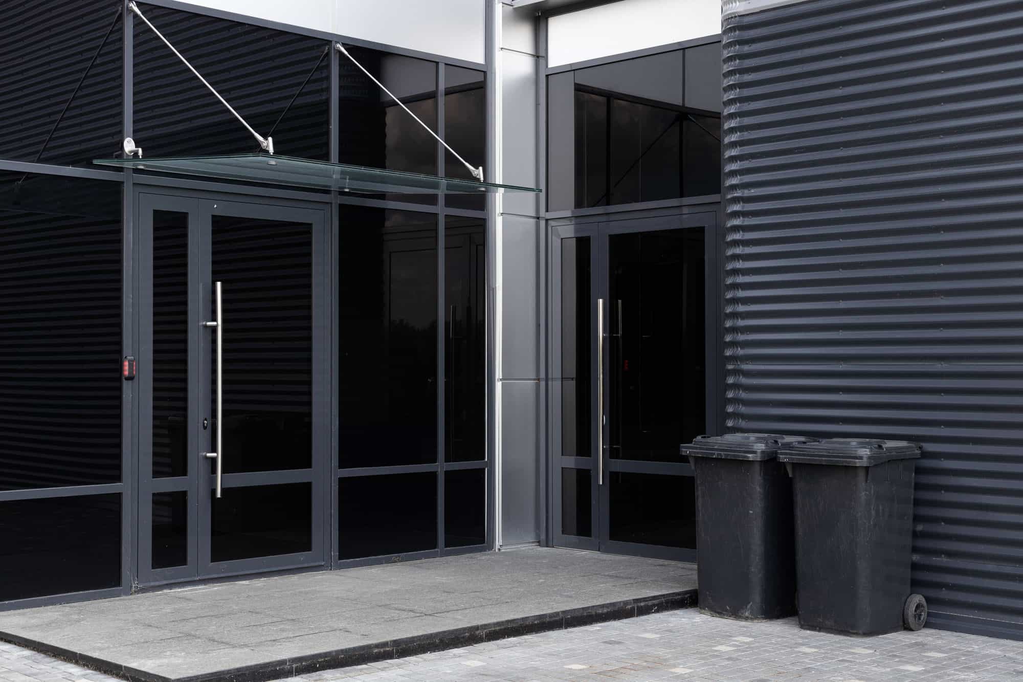 Commercial wheelie bins beside the glass entrance of a modern business unit Commercial wheelie bins beside the glass entrance of a modern business unit