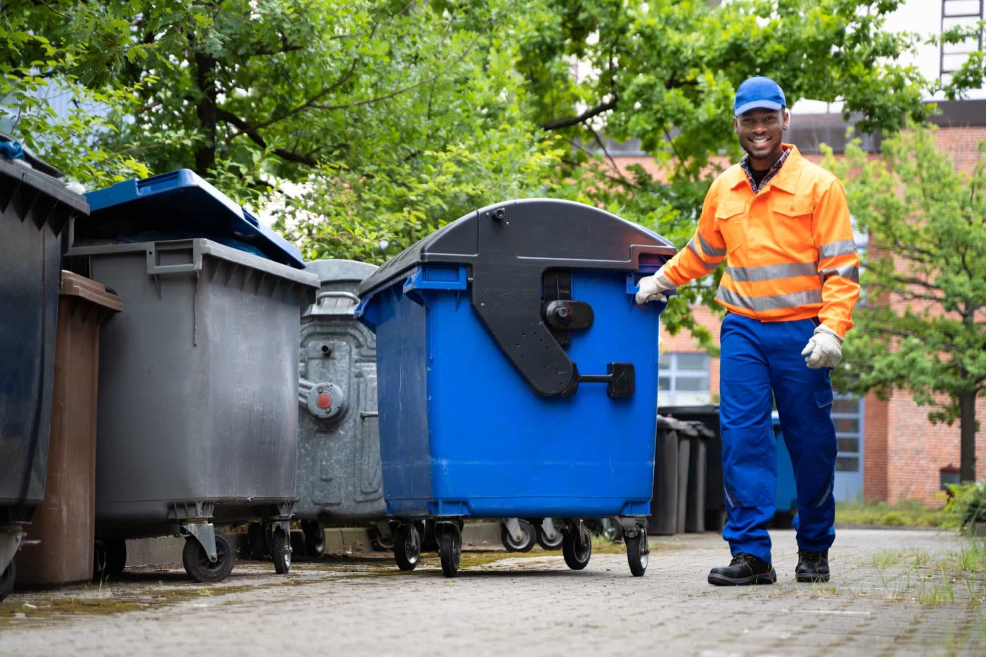An operative in hi-vis workwear wheeling a communal waste bin into line An operative in hi-vis workwear wheeling a communal waste bin into line
