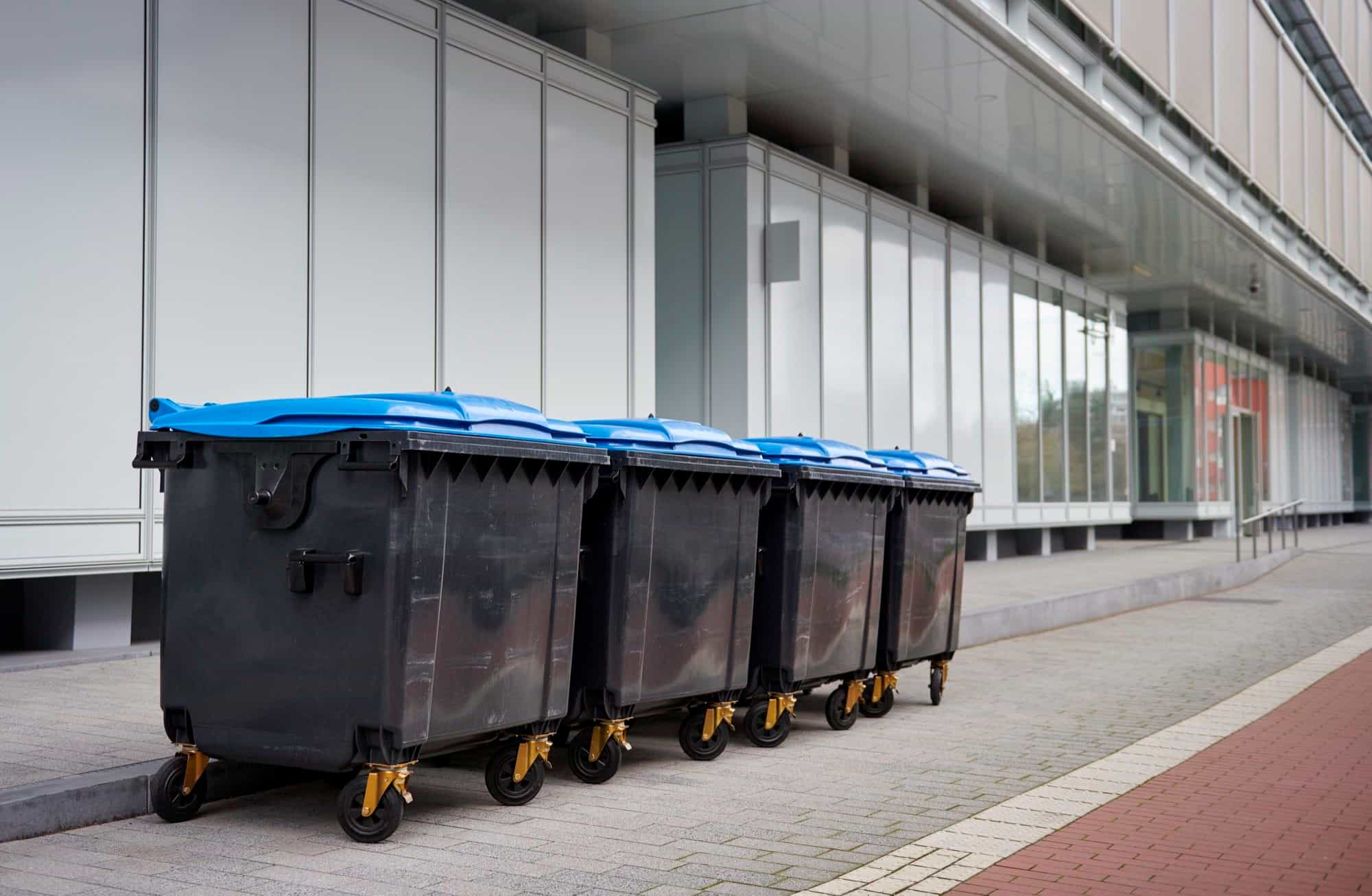 A row of commercial waste containers with blue lids outside business premises A row of commercial waste containers with blue lids outside business premises